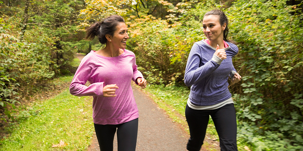Mother and daughter smiling while running through countryside Mother and daughter smiling while running through countryside